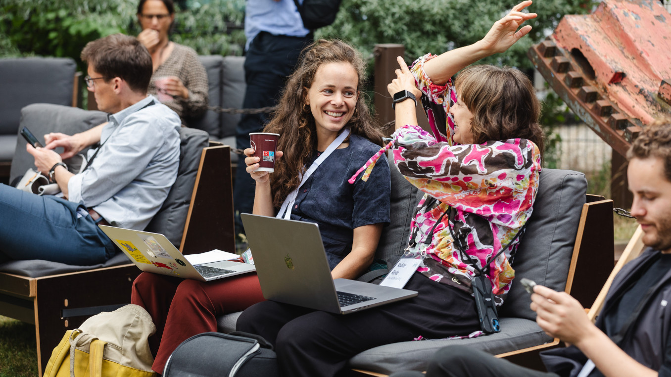 two woman at the festival sitting with the laptops talking and smiling 